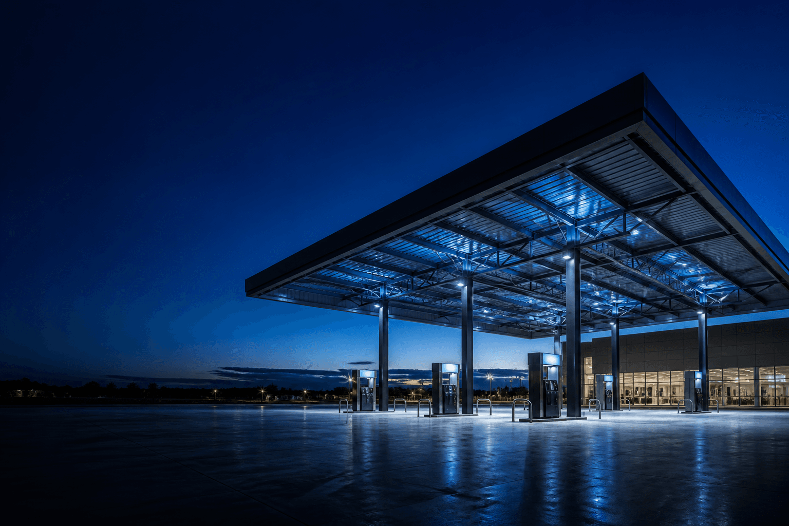 Night canopy and forecourt of a completed petrol station, lit in navy and sky blue