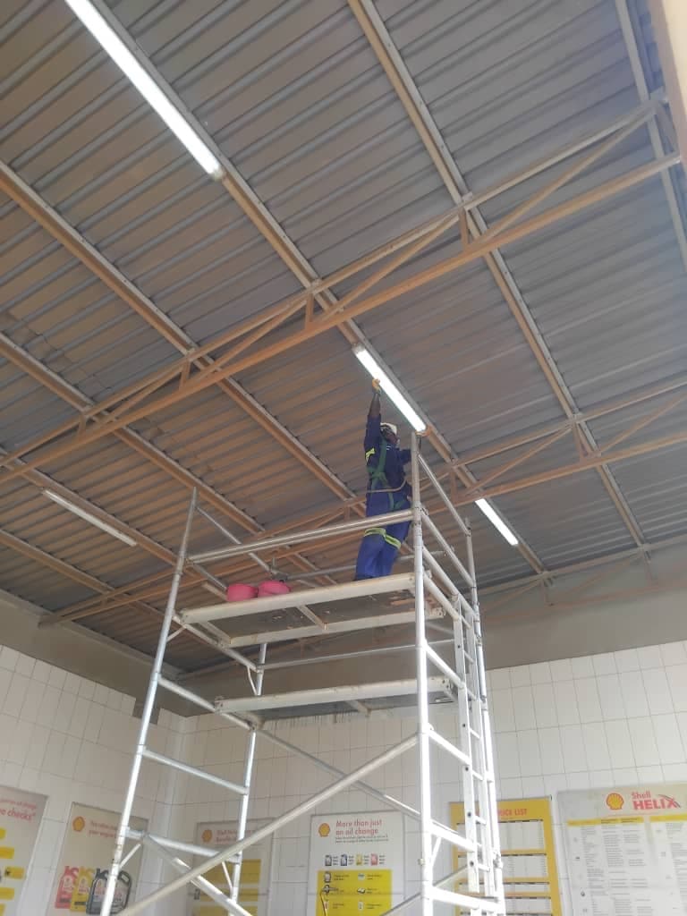 Safety-harnessed technician working at height on a station ceiling